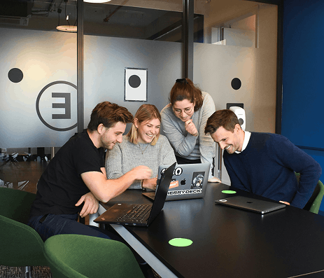 Four employees gathered around a laptop in an office, enthusiastically collaborating on a workplace challenge